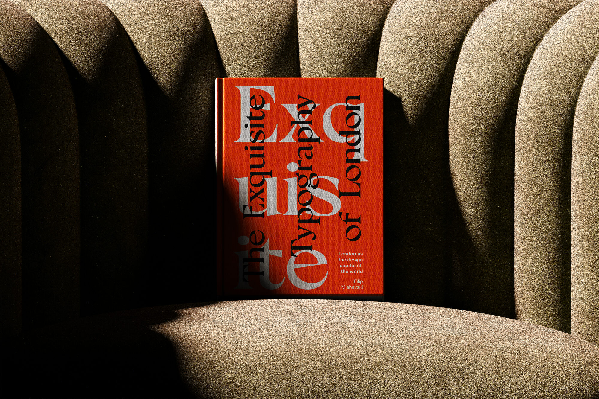 The cover mockup standing on a ribbed fabric armchair: The Exquisite Typography of London set in overlapping grey and black serif letters on red, subtitled London as the design capitol of the world.