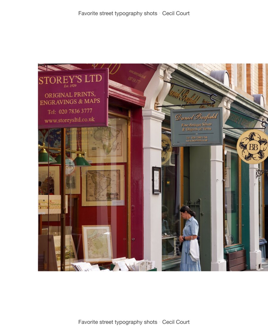 Storey&rsquo;s Ltd, original prints, engravings and maps, lettered in gold on a deep pink shopfront, with David Brass antiquarian books in gold on green beside it and a woman looking into the window.