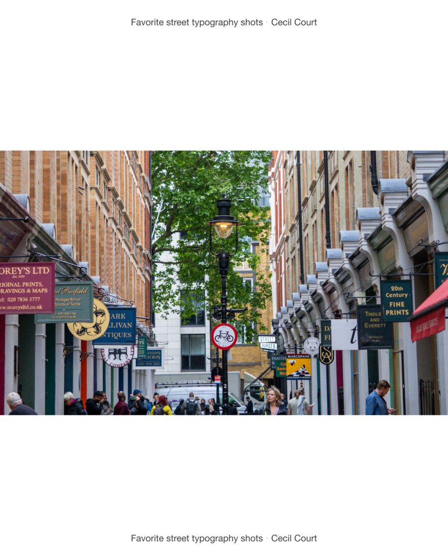 The length of Cecil Court, hanging signs down both sides, a lamp post in the middle of the row and people walking between the shopfronts.
