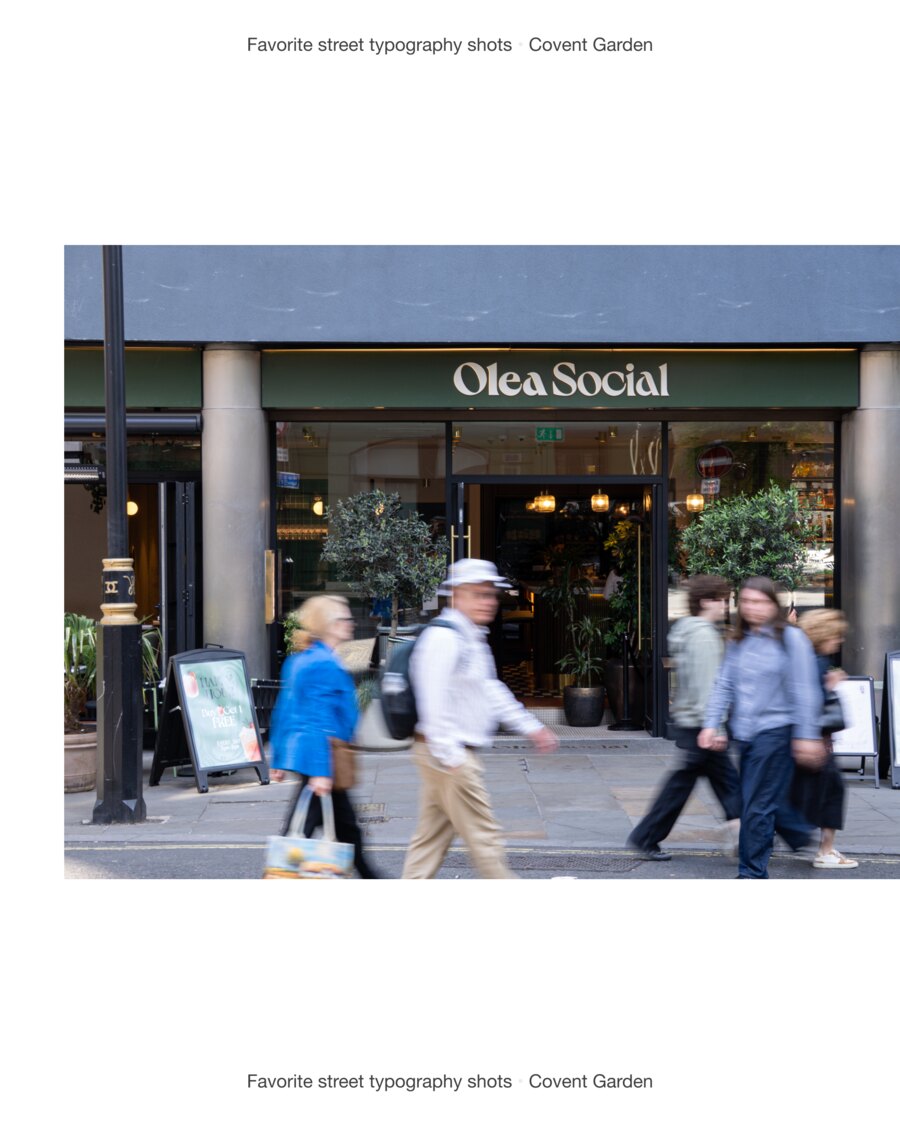 Olea Social lettered in a pale rounded serif across a deep green fascia, with people blurred as they pass the open doors and olive trees either side.