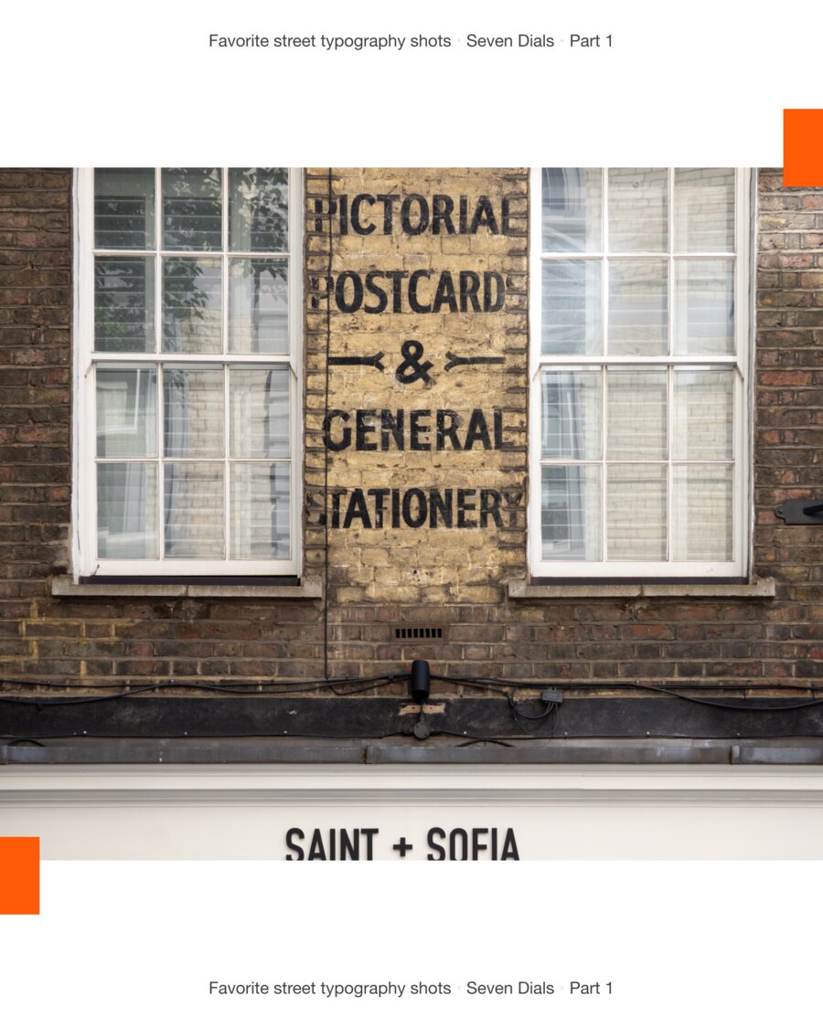 A faded painted ghost sign on bare brick between two sash windows, reading Pictorial Postcard and General Stationery, above a modern Saint + Sofia fascia.