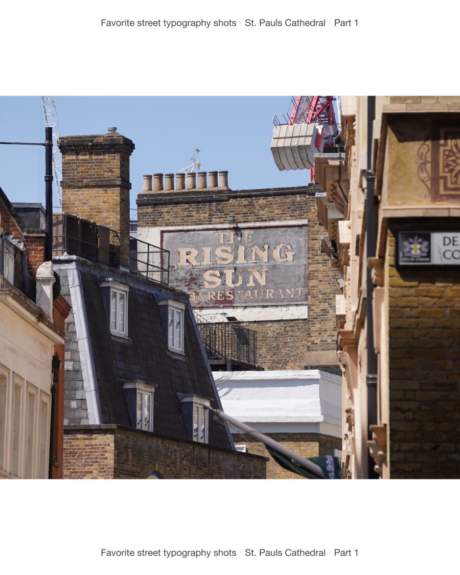Rooftops and chimneys, with a painted ghost sign on a brick flank wall reading The Rising Sun Restaurant.