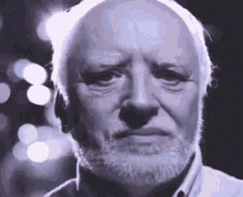 A grey-haired, white-bearded man in close-up smiling with visible strain against a backdrop of bokeh lights &mdash; the stock photograph known as Hide the Pain Harold.